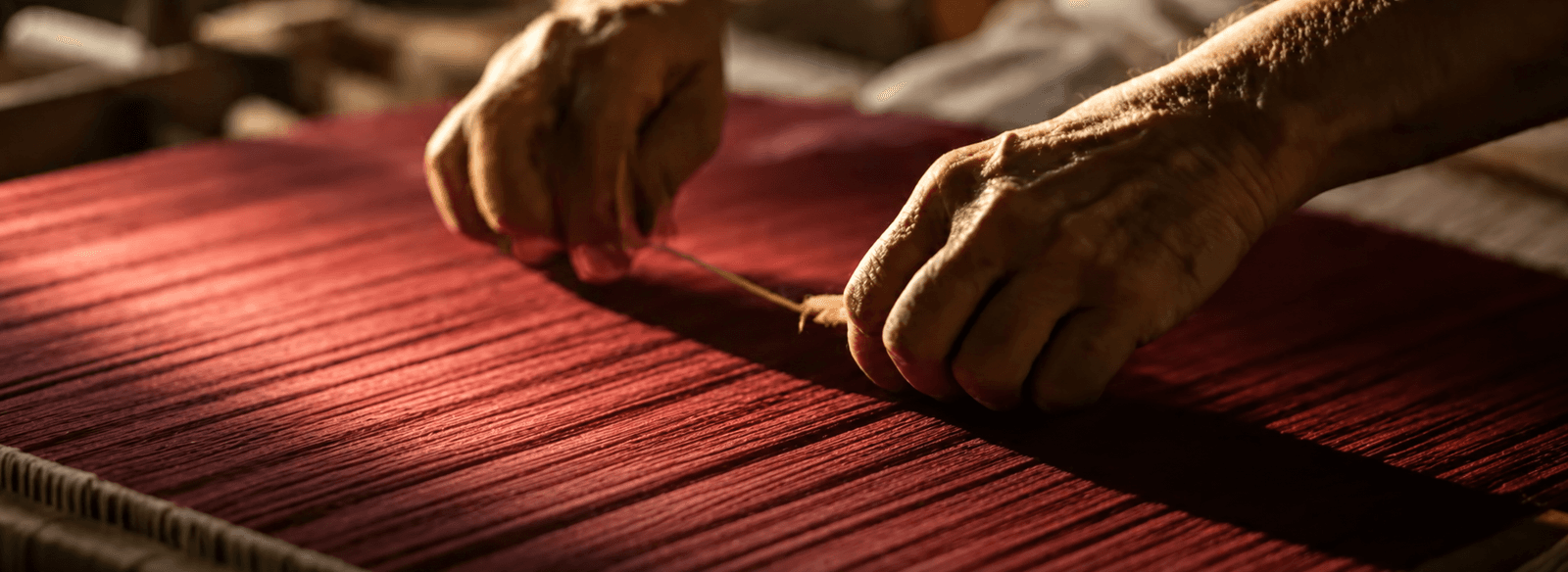 Artisan hands weaving red fabric on a loom